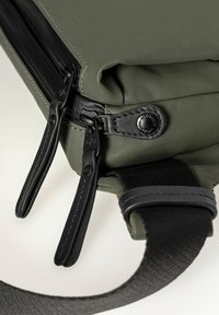 Groene stoffen tas met zwarte ritsen en hardware. Heeft een gestructureerde schouderband en een glad oppervlak, wat een eenvoudig en functioneel ontwerp laat zien.