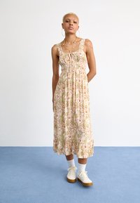 Florale maxi-jurk met een fitted bodice, elastische taille en uitlopende zoom. Lichtroze, groene en crèmekleurige tinten met een geribbelde afwerking aan de onderkant.