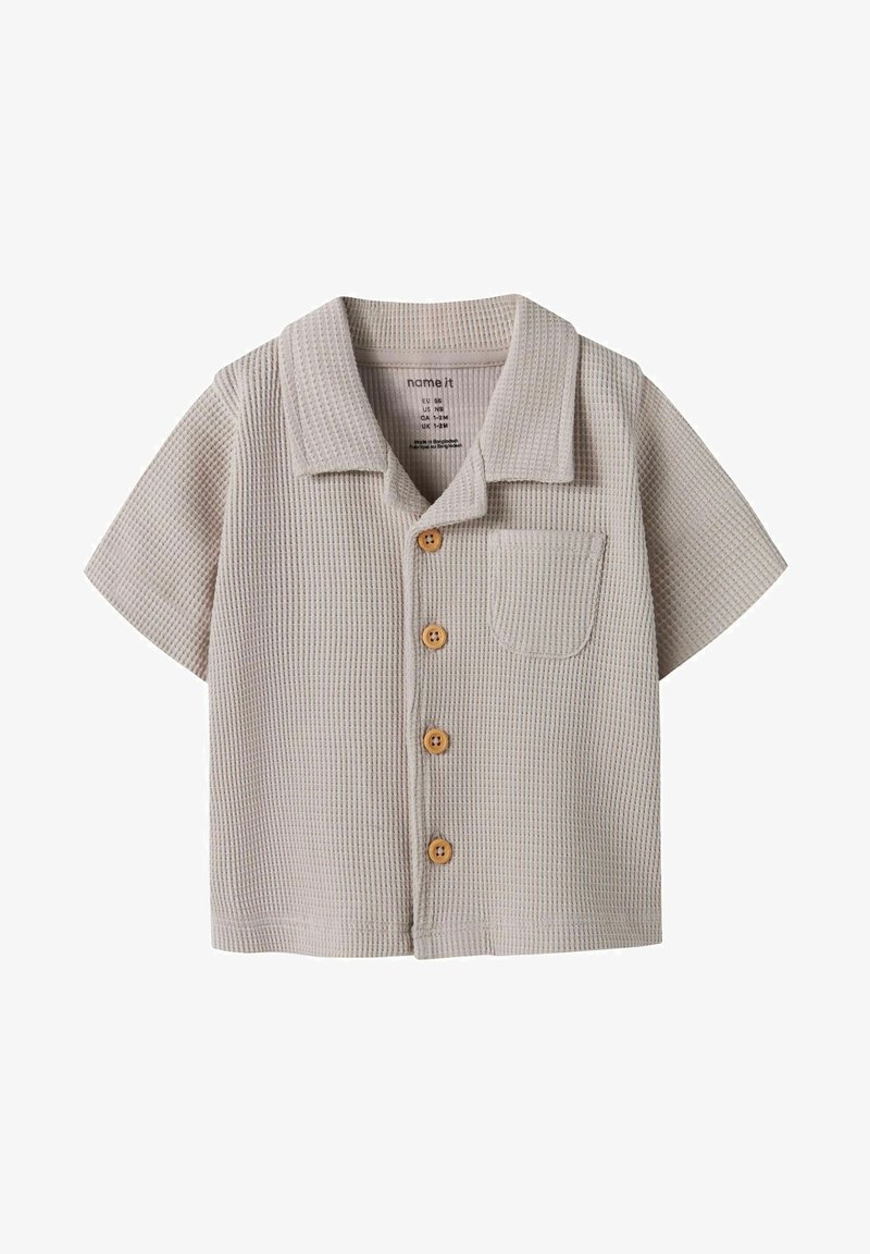 Chemise beige à manches courtes pour tout-petit en maille gaufrée, avec des boutons en bois et une petite poche poitrine, dotée d'un col camp.