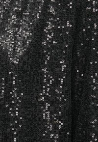 Crna tkanina s teksturiranom površinom, ukrašena srebrnim šljokicama različitih veličina, stvarajući blistav efekt.