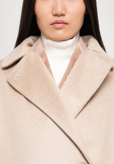 Beige wool coat with a wide collar, featuring a textured surface and a striped inner lining. Worn over a white turtleneck.