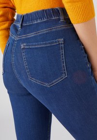 Jeans de mezclilla azul con una cintura alta, que presentan dos bolsillos traseros y costuras en contraste. El material parece suave y con un ligero estiramiento.