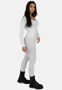Bodysuit blanco de manga larga acanalado con escote redondeado, combinado con botas de combate negras con cordones, que enfatizan una silueta ajustada.