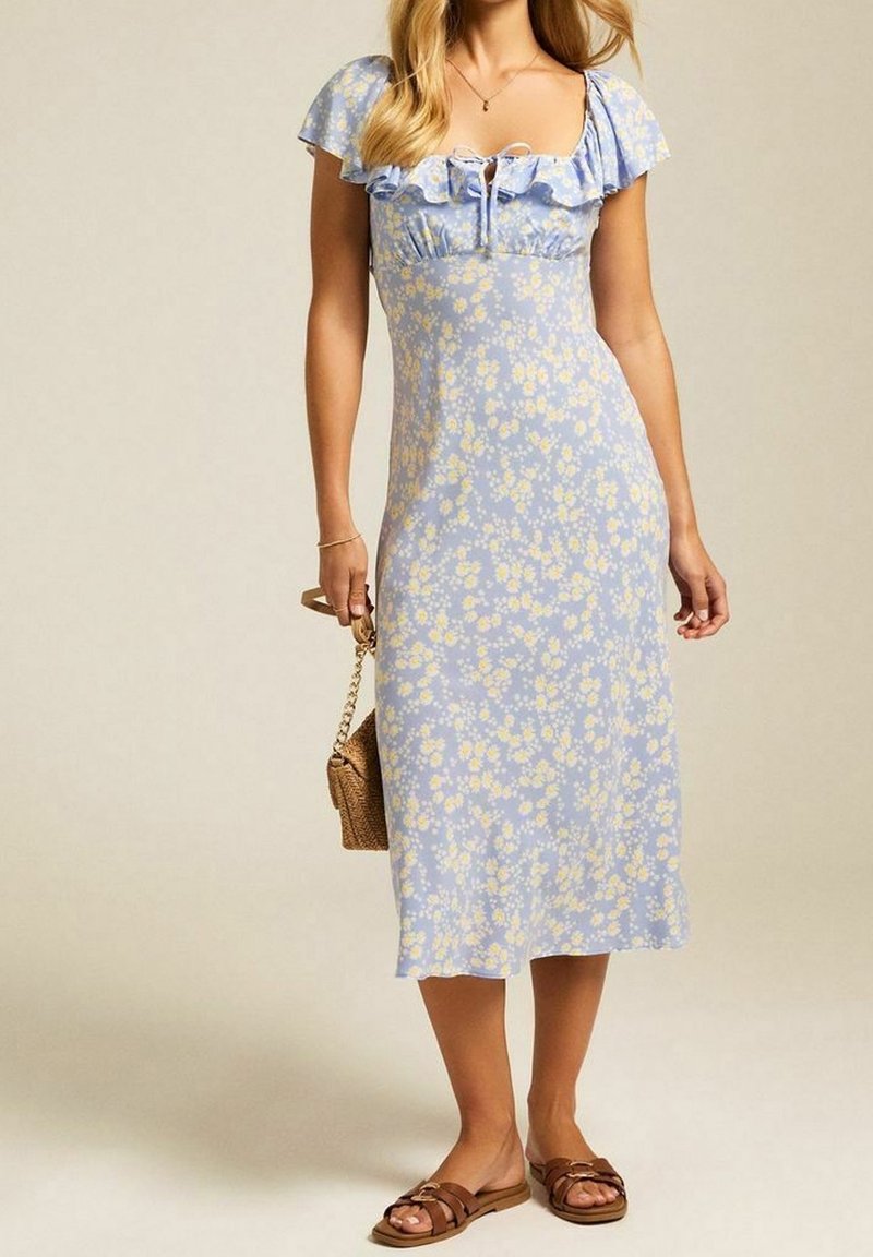 Vaaleansininen kukkamekko, jossa on lyhyet röyhelöhalkaisut, neliön muotoinen kaula-aukko ja tiukka yläosa. Mekossa on ilmava siluetti ja korostettu vyötärö.