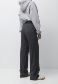 Sudadera gris con capucha combinada con pantalones de pierna ancha de rayas oscuras. Los pantalones presentan un corte entallado y un sutil detalle de bolsillo trasero.