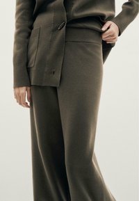 Pull en maille vert olive avec fermeture à boutons et poignets côtelés, assorti à un pantalon large assorti. Texture douce, coupe décontractée.