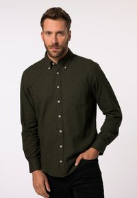 Camisa abotonada de un verde oscuro hecha de una tela texturizada, con un bolsillo en el pecho y botones blancos, combinada con pantalones negros.