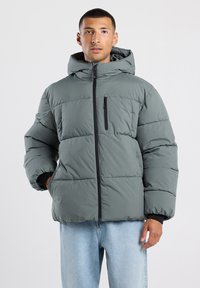 Chaqueta acolchada gris con capucha, que cuenta con un cierre delantero, bolsillos laterales y un bolsillo con cremallera en el pecho. Material grueso y acolchado con un acabado suave.