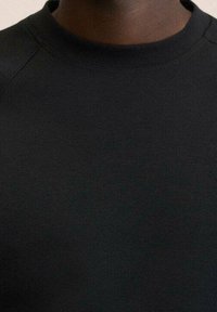 Sort crewneck sweatshirt lavet af struktureret stof med en glat finish og raglanærmer, med et minimalistisk design uden udsmykninger.
