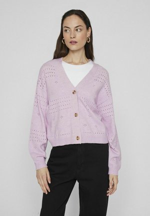 Lichte roze cardigan met V-hals, knopen aan de voorkant en gebreid patroon. Heeft geribbelde manchetten en zoom, gedragen over een wit T-shirt en zwarte broek.