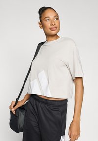 Šviesiai pilkas trumpintas marškinėlis su trumpomis rankovėmis, priekyje su baltomis abstrakčiomis detalėmis. Derinamas su juodomis sportinėmis kelnėmis ir maža rankine.