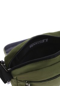 Bolso de hombro de tela verde con cierre de cremallera, con un interior negro y etiqueta de logo. Incluye una correa ajustable y superficie texturizada.