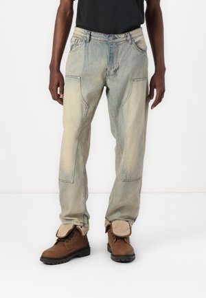 Homme portant un pantalon en jean clair délavé et des bottes marron à lacets avec des revers pliés en laine beige.