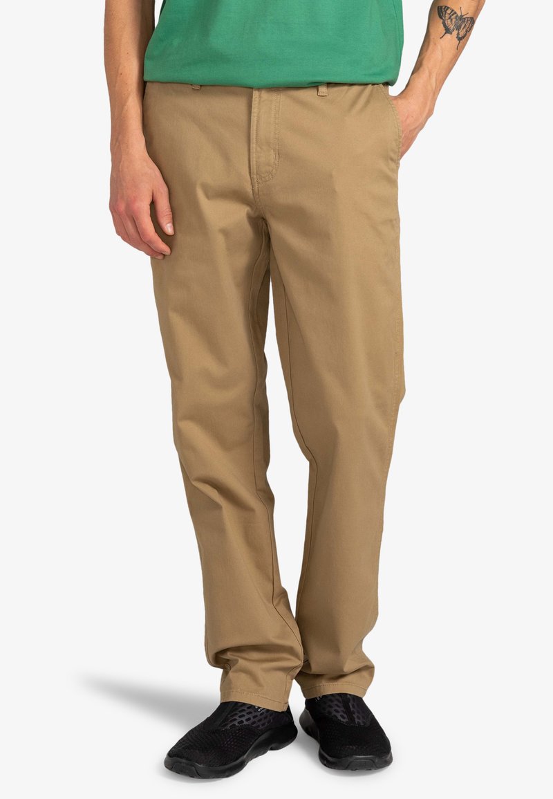 Beige bomulds chinos med lige ben design, der har sidelommer og en subtil tekstur. Sammen med sorte træningssko.
