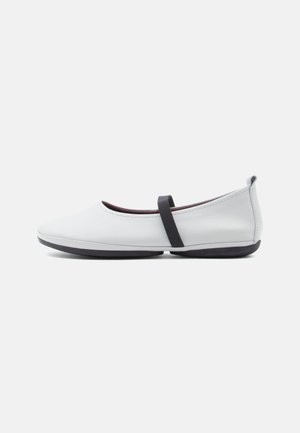 Hvite ballettsko i glatt skinn, med lav profil, rund tå og en svart elastisk stropp over vristen.