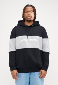 Zwarte en grijze hoodie met een voorke pocket, trekkoorden en een logo-opdruk. Heeft een kleurblokontwerp met een zachte textuur.
