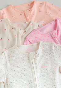 Neljän ryppyisen vauvan univaatteen setti, jotka ovat väriltään vaaleanpunainen, kerma, valkoinen ja persikka, ja joissa on pieniä kirsikka- ja sydänkuvioita, aseteltuna limittäin tasaiselle pinnalle.