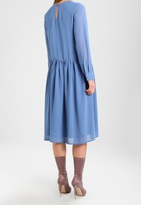 Robe en chiffon bleu avec des manches longues, un dos en trou de serrure et une taille froncée, associée à des talons roses clairs et des chaussettes assorties.