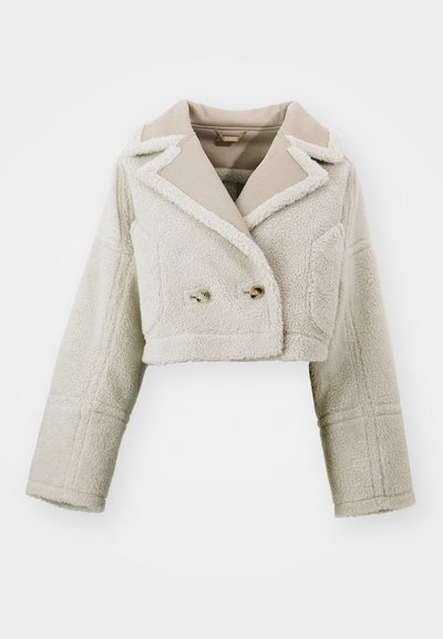 Κοντό σακάκι σε ανοιχτό μπεζ, με υφή φανελένιου υφάσματος, αντίθετο λείο γιακά, διπλό εμπρός κλείσιμο και δύο πλαινές τσέπες.