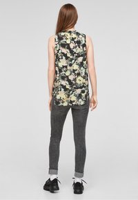 Hladká černá bezramenná blůza s květinovým vzorem a pastelovými akcenty, zkombinována s tmavě šedými skinny džíny a černými teniskami s bílými ponožkami.