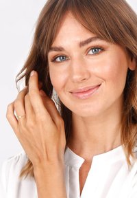 Goldener Ring mit einem kleinen Perlen-Detail, getragen an der Hand. Das Model hat hellbraune Haare und trägt eine weiße Bluse mit einem dezenten Kragen.