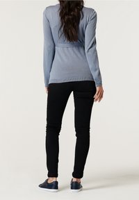 Haut à manches longues bleu clair avec taille ajustée, associé à un jean skinny noir et des baskets bleu marine. Tissu texturé et détails de design simples.