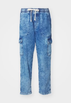 Helleblaue Denim-Cargo-Hosen mit elastischem Bund, Kordelzugverschluss und zwei Seitentaschen. Mit einer einzigen Cargo-Tasche am linken Bein.