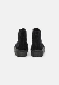 Bottines chelsea en suède noir avec un dessus texturé, des panneaux latéraux élastiques et une semelle épaisse en caoutchouc noir. Présente un petit logo sur le talon.