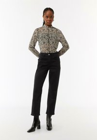 Black high-waisted jeans paired with a long-sleeve, patterned blouse featuring a button-up front. Model wearing black ankle boots.