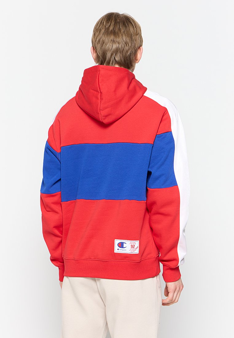 Felpa con cappuccio in blocchi di colore rosso, blu e bianco, con tasca a marsupio frontale, cappuccio e patch con logo in basso. Tessuto morbido, vestibilità comoda.