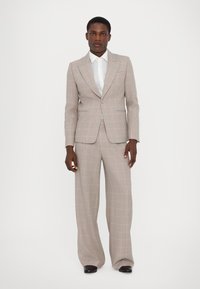 Šviesiai pilkas kostiumas su rožinės spalvos raštu, apimantis pritaikytą švarką ir plačius kelnes. Pora su balta marškiniai su apykakle.