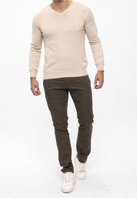 Beige v-halstrui gecombineerd met olijfgroene broek en witte sneakers. De trui heeft een zachte textuur; de outfit heeft een casual stijl.