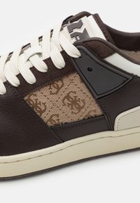 Sneaker in pelle marrone con tessuto a motivo beige, lacci avorio e dettagli neri. Pannello laterale testurizzato e suola in gomma crema.