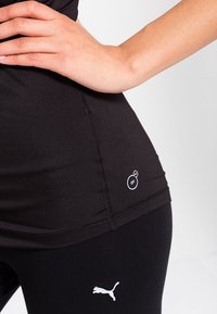 Černý sportovní top s funkcí odvodu vlhkosti, bezšvovým designem a malým bílým logem; spárován s černými legínami, které mají bílé logo.
