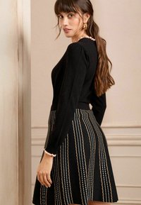 Top negro de manga larga con cuello volcado, combinado con una falda negra con estampado que presenta rayas verticales en crema y dorado.