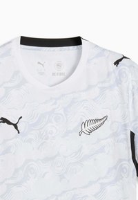 Maillot de sport blanc avec un motif subtil de nuages tourbillonnants, logos Puma noirs sur la poitrine et les manches, et emblème de fougère noir et blanc sur la poitrine.