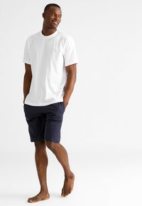 Witte t-shirt met korte mouwen, gecombineerd met marineblauwe shorts. De t-shirt heeft een ronde hals, en de shorts hebben een elastische tailleband.