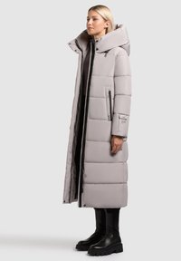 Cappotto lungo grigio imbottito con colletto alto, zip frontale e tasche laterali. Presenta una texture trapuntata e un design elegante.