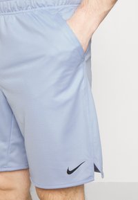 Pantalones cortos deportivos azul claro con cintura elástica, bolsillos laterales y un logo negro de Nike en la parte inferior izquierda. Textura de tela suave.