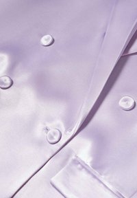 Gros plan sur un tissu satin violet clair avec une finition brillante, montrant des boutons ronds cousus et une couture ajustée.