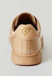 Beige patent leather sneaker with a textured sole, featuring a gold triangular "Guess" logo on the back and rounded heel design.