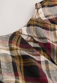 Tessuto a quadri con tonalità di nero, giallo, grigio e bordeaux in una trama tessuta con dettaglio di bottone sul collo.