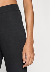 Μαύρο ριμπ κολάν με ελαστική μέση. Απαλή υφή και εφαρμοστό σχέδιο. Χέρι τοποθετημένο δ ίπλα στο κολάν, εμφανίζοντας φυσικό τόνο δέρματος.