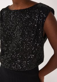 Top nero a paillettes con scollatura a barca, maniche corte e tessuto testurizzato. Presenta una gonna nera a coste aderente nella parte inferiore.