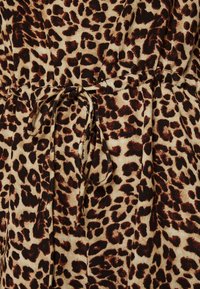 Tissu à imprimé léopard avec des taches brunes et noires sur un fond beige. Présente un détail de taille nouée, une texture douce et un design drapé.