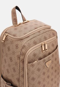Beige canvas rugzak met een reliëflogo-patroon, dubbele ritsen, een handvat aan de bovenkant en een voorvak met een gouden hardware-accent.