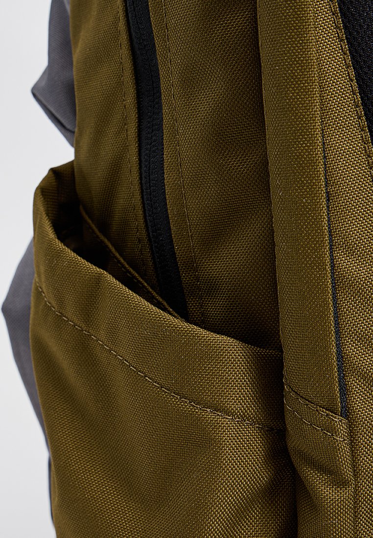 Nahaufnahme einer khakifarbenen Stoffrucksacktasche mit schwarzem Reißverschluss und verstärkten Nähten an der Seite und der Vorderseite.