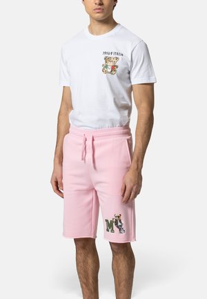 Mann trägt weißes T-Shirt mit Teddybär und dem Text "1969 Italia" sowie pinke Shorts mit einem Teddybär, der Fußball spielt, und dem Buchstaben "M".