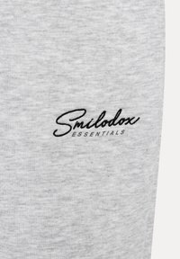 Graue Sweatpants mit einer weichen Textur und einem gestickten schwarzen Logo, das auf der linken Seite "Smilodox ESSENTIALS" liest.