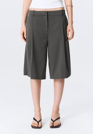 Grijze krijtstreep brede broekshorts tot op de knie, gedragen door een persoon met zwarte, vierkante sandalen en een wit cropped topje.